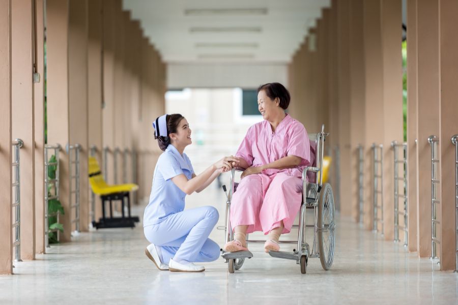 image presents elder woman smiling in a wheelchair with a nurse smiling having facing each other